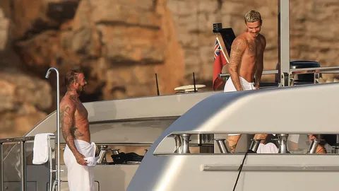 Shirtless Romeo Beckham, 23, looks just like his famous dad David, 51, as they show off their tattooed torsos in matching towels - after trolling Cruz for those tight white pants in Ibiza